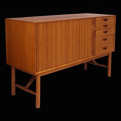 Peter Hvidt & Orla Mølgaard-Nielsen: Teak 
sideboard with five drawers and a rolling door.
A small scratch at the lower right front. 
Designed 1956. H: 87cm. L: 135cm. D: 48cm