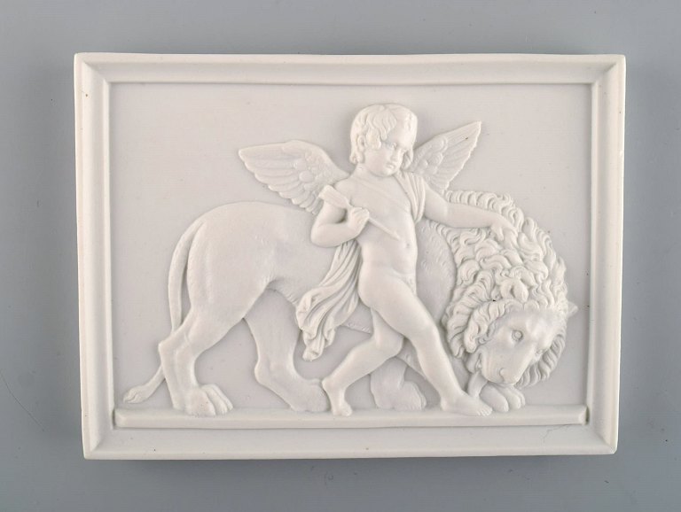 Bing and Grøndahl after Thorvaldsen. Antique biscuit wall plaque with puti and 
lion in relief. 1870 / 80s.
